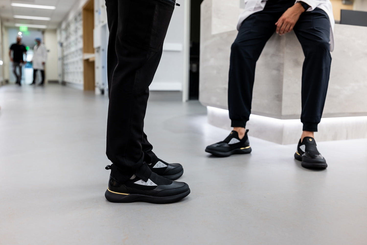 Two healthcare colleagues in a clinic corridor wearing black Snogs sneakers