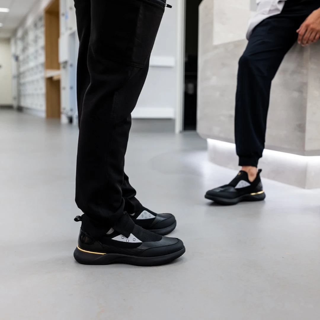 Two healthcare workers in black Snogs Genesis Night Shift sneakers in a hospital corridor